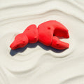 Red keychain shaped like a lobster claw on sandy beach